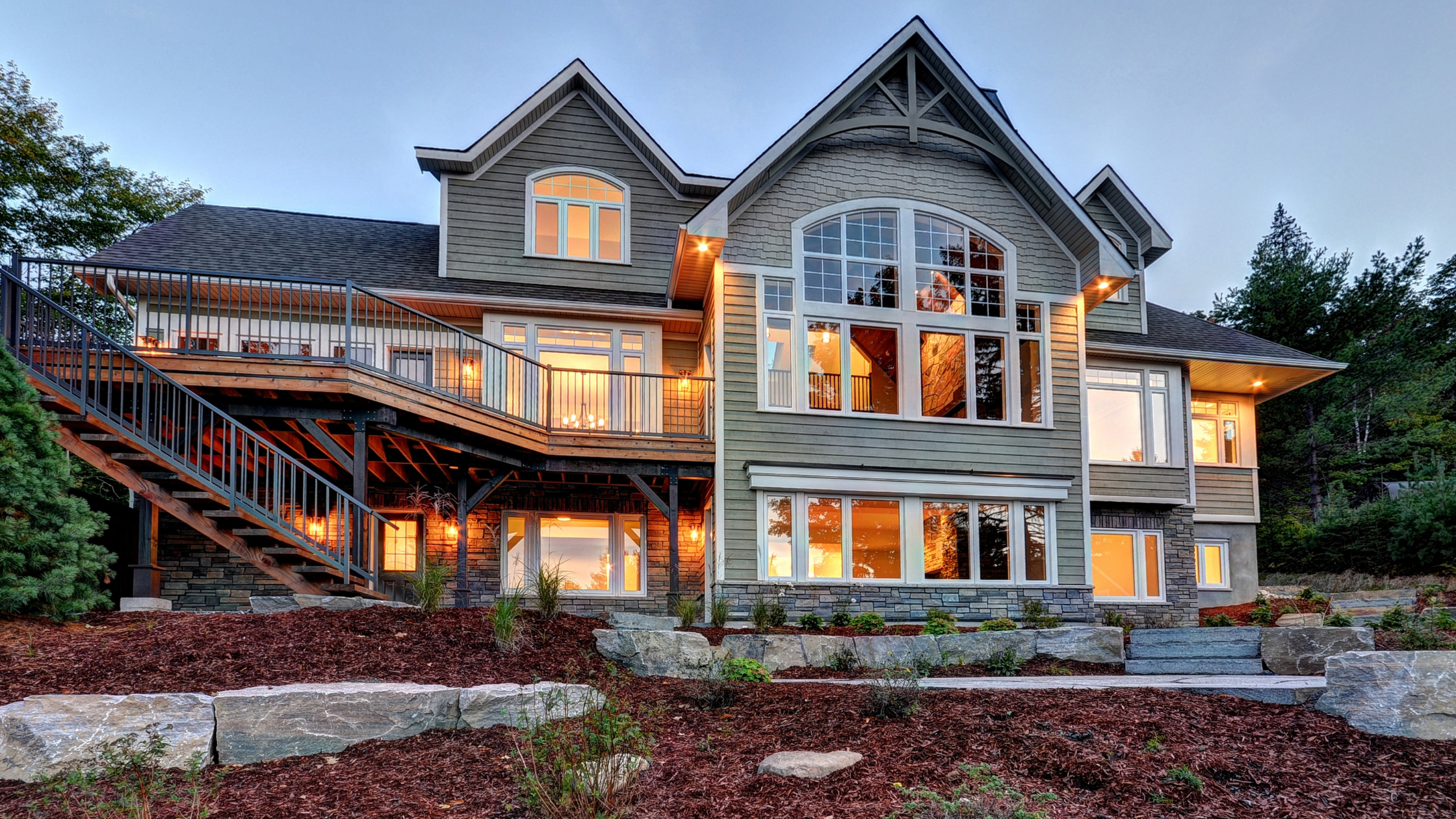 Multi-level custom cottage in Muskoka with wraparound decks, mixed stone and wood siding, and complex rooflines showcasing architectural features that influence the cost to build a custom cottage in Muskoka