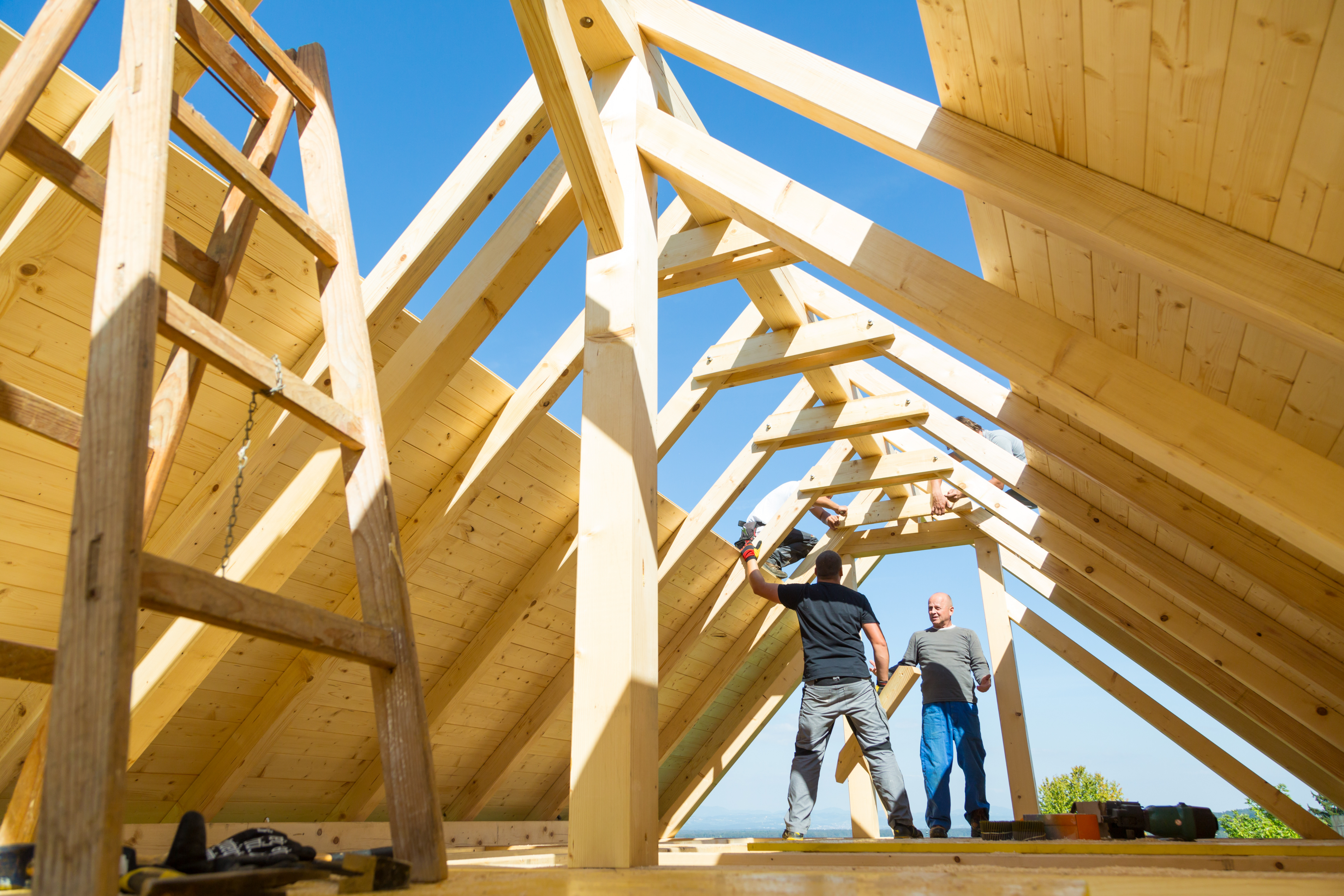 Construction crew framing a custom roof structure, illustrating the need for builder’s risk insurance during early stages of a home build.